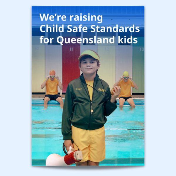A young person in a coach's jacket and yellow shorts stands by a pool, holding a megaphone, with two swimmers in the background adjusting their goggles.